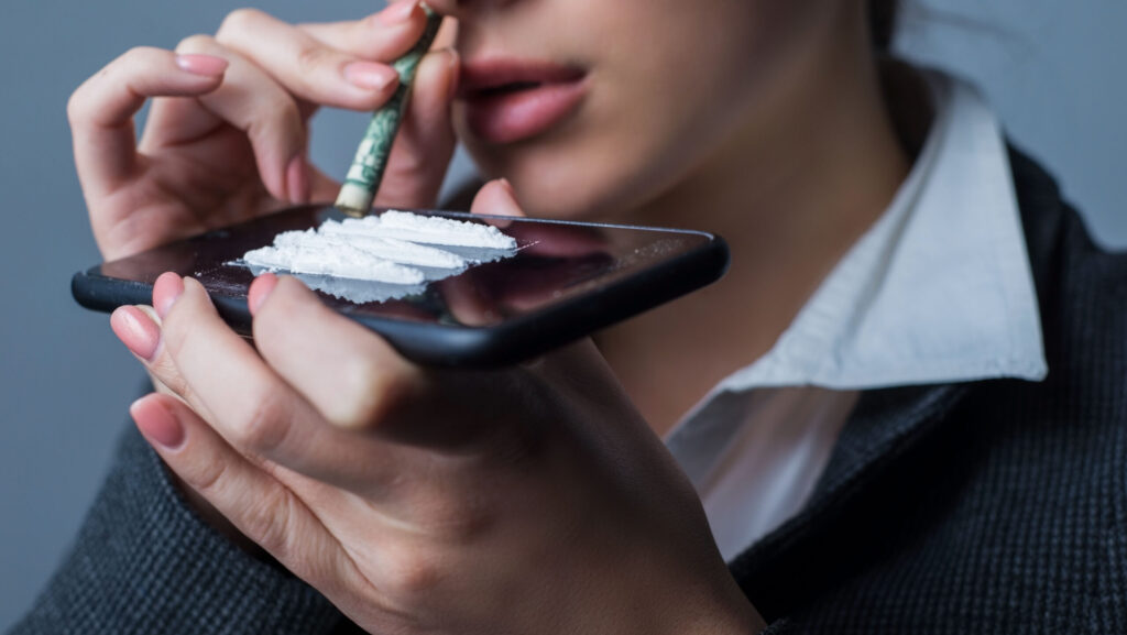 A young women snorting cocaine off her phone anticipating experiencing coke bloat.