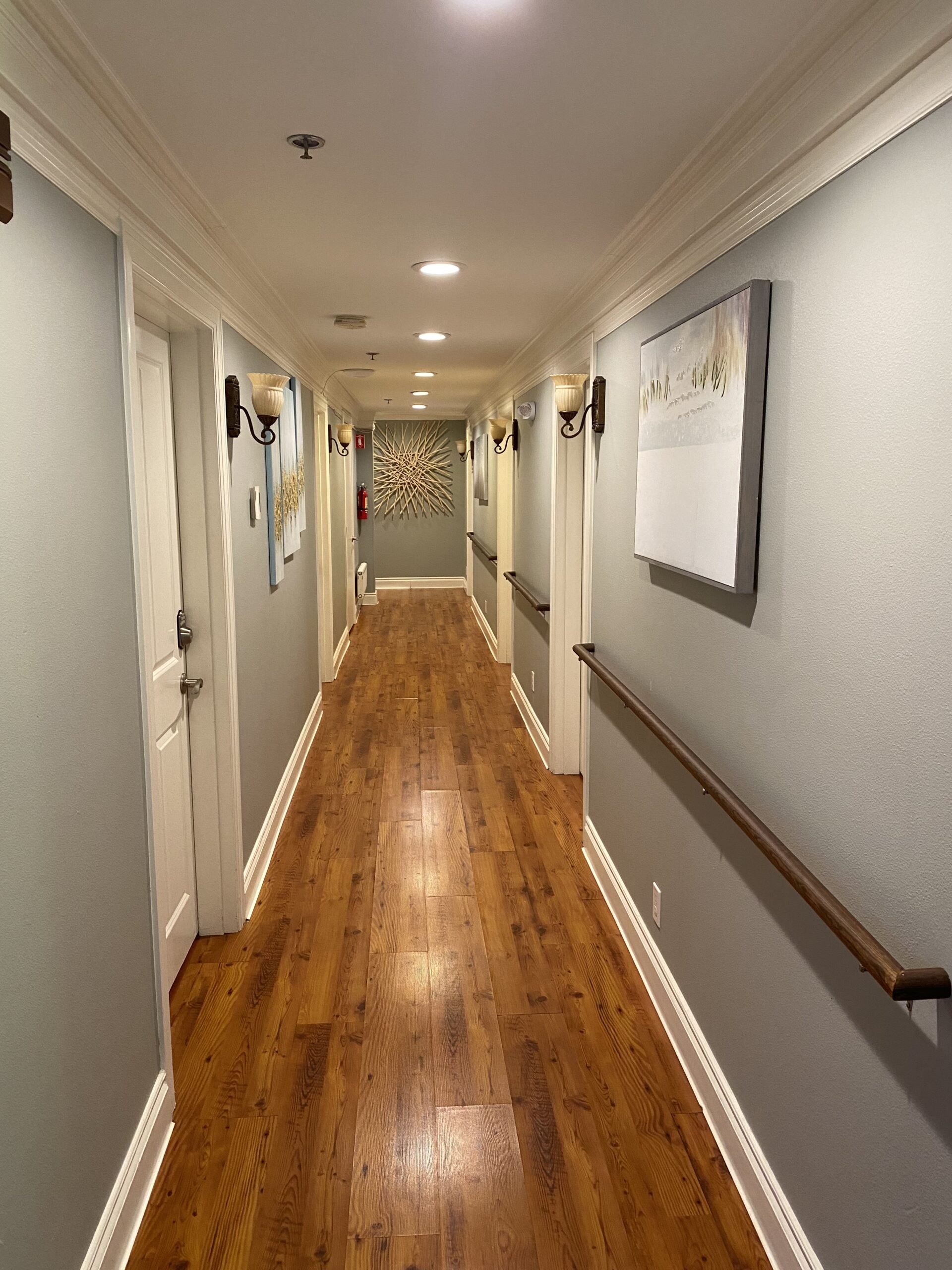 Hallway of Hotel California by the Sea's Detox home, with hardwood floors, white molding, decorative sconces, and art on the walls