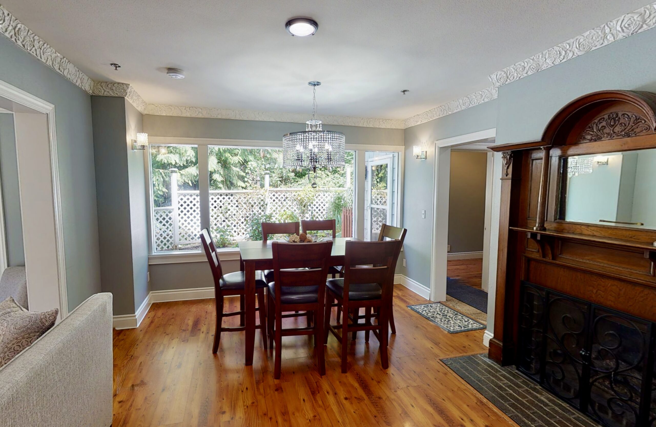 interior of dining room, with white floral molding, an old ornate fireplace, with wood carving, a mirror, brick surrounding it. Theres a crystal chandelier and a wood table with 6 chairs