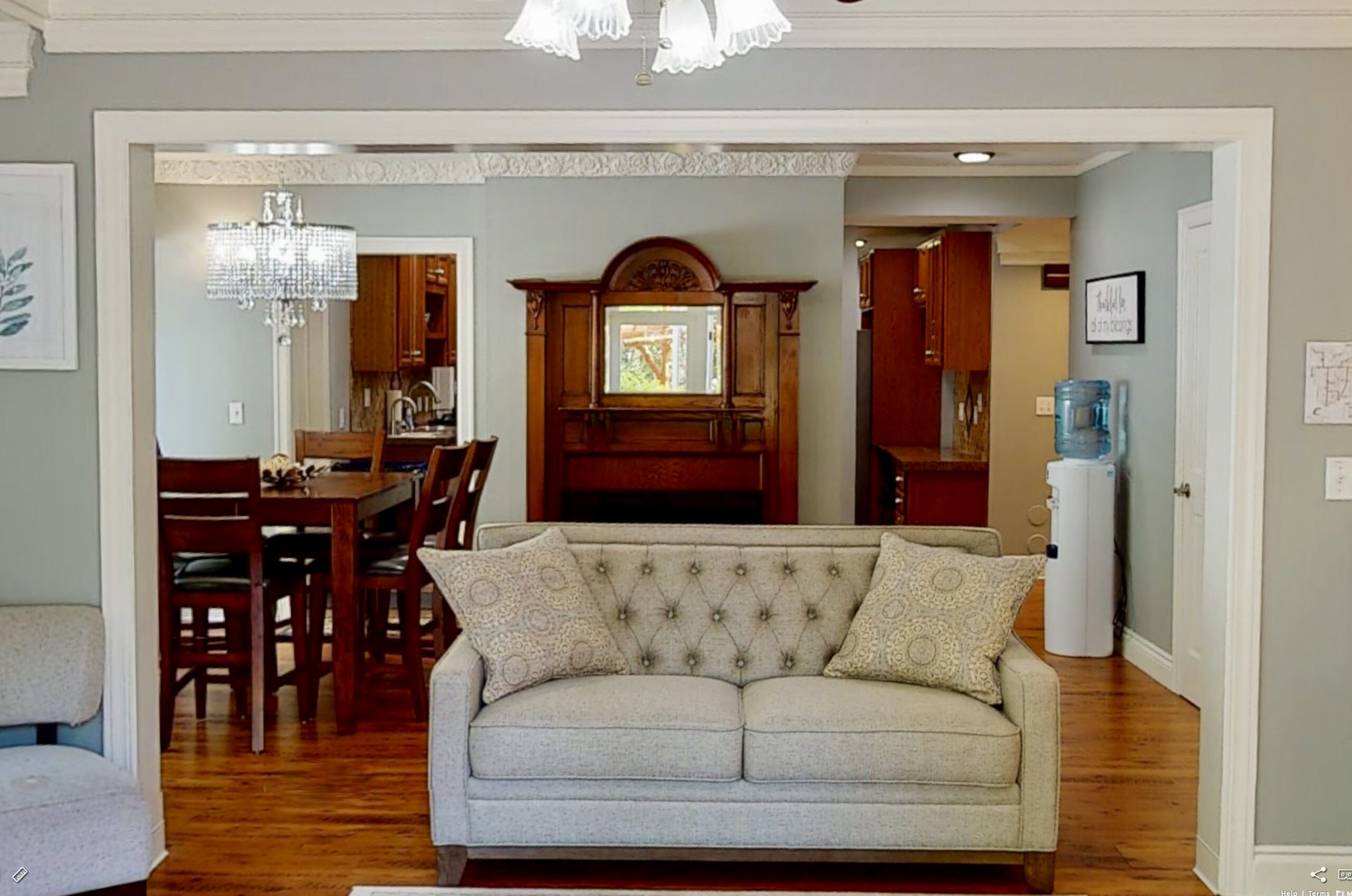 Interior of Kirkland detox home, living room with a grey couch, ornate pillow, white molding, an open airy sitting area with the dining table in the back