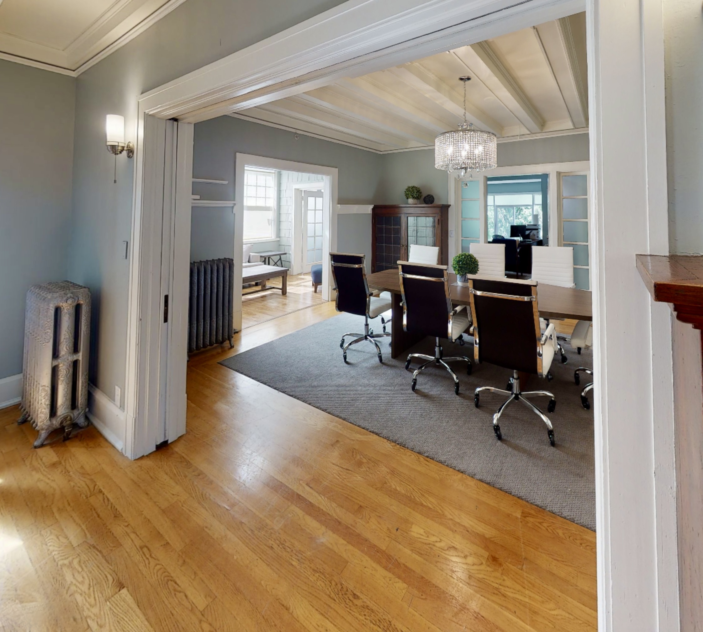 interior of dining room, with white molding, crystal chandelier and a wood table with 6 office chairs. Open floor plan shows two other clean, airy rooms