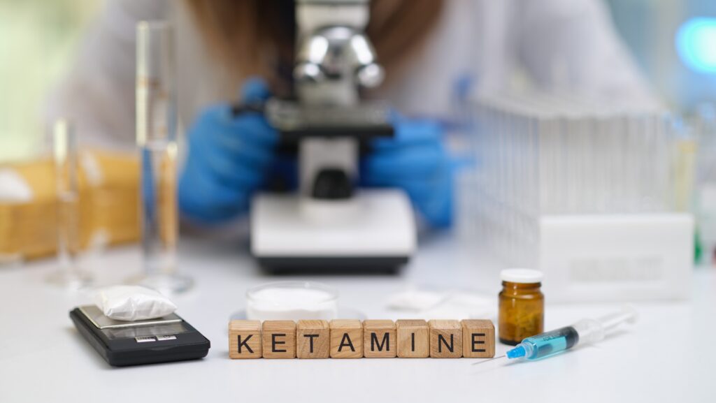 Blocks spelling out the word ketamine next to a drug scale and syringe.