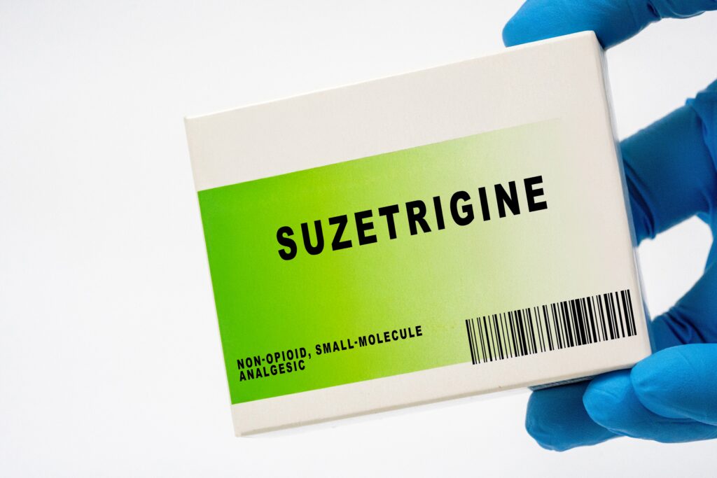 A gloved hand is holding a white and green medication box of suzetrigine, a non opioid analgesic.