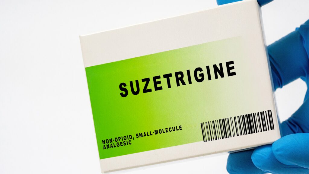 A gloved hand is holding a white and green medication box of suzetrigine, a non opioid analgesic.