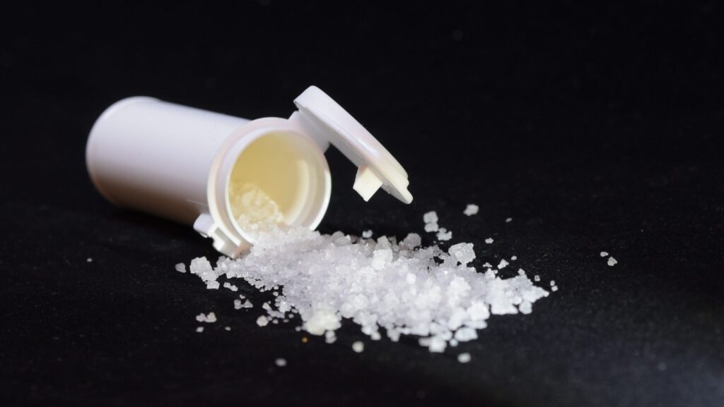 A white spilled over bottle of chunks of crystal meth on a black background.