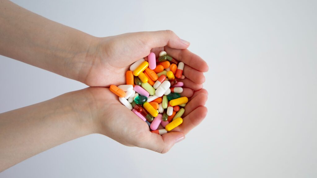 A person with a handful of colorful pills represents signs someone is addicted to pain pills.