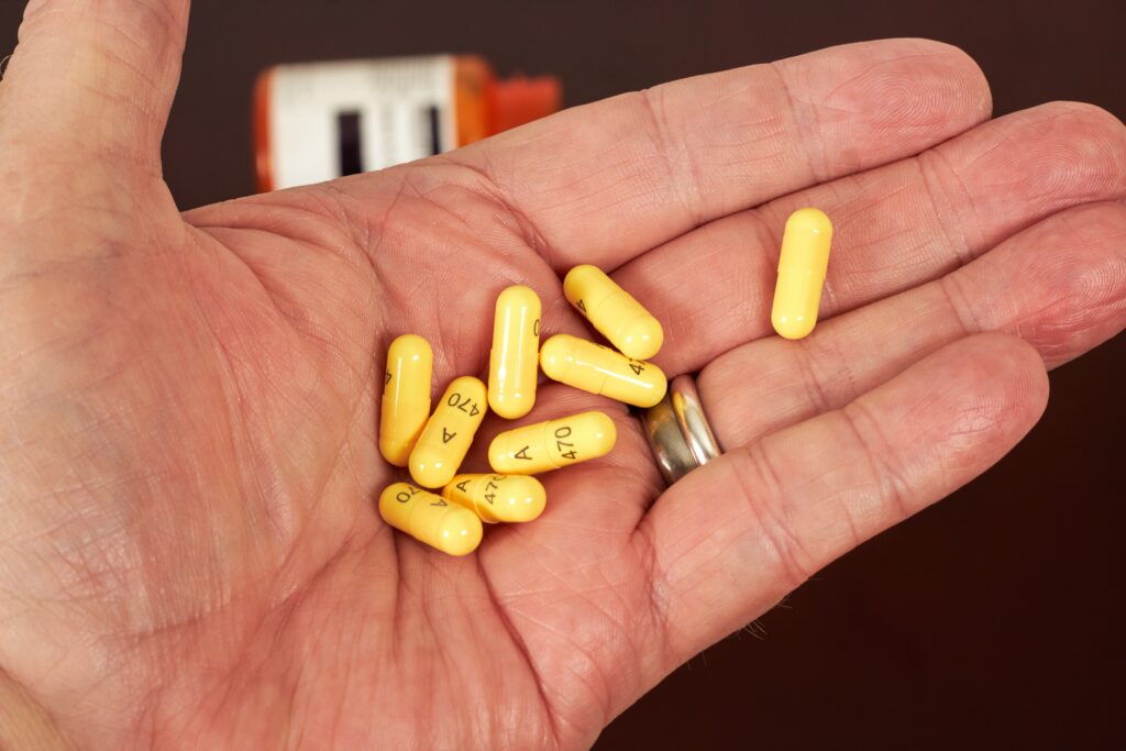 In the palm of a man's hands, he is holding yellow capsules of gabapentin for opioid withdrawal symptoms.
