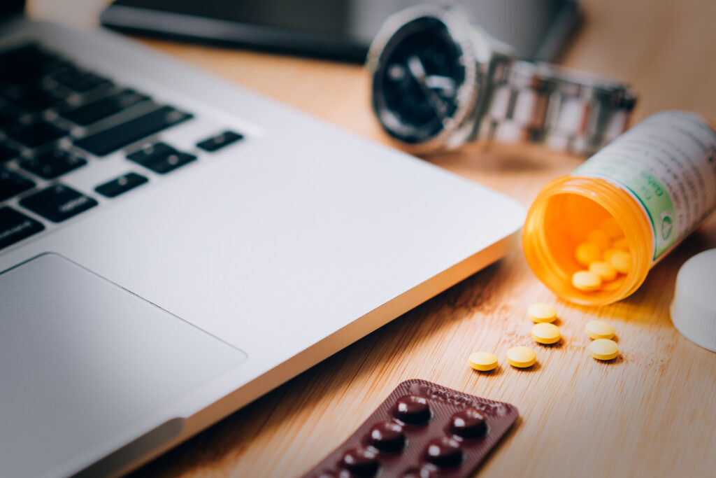 A prescription bottle of pills is spilled out next to a laptop representing trazodone withdrawal.