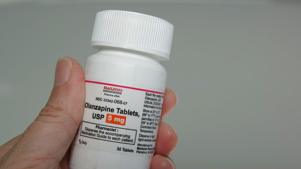 A white prescription bottle of olanzapine, which if abused can lead to olanzapine withdrawal symptoms.