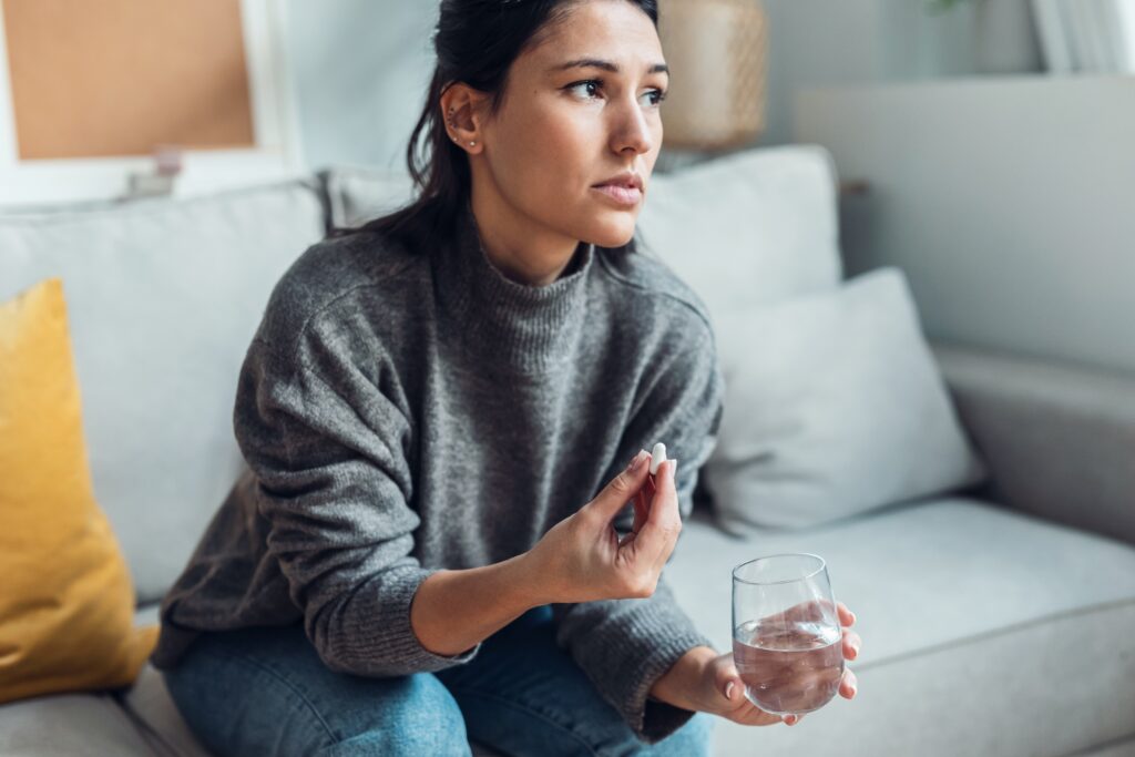A young woman holding an antidepressant pill and a glass of water is experiencing slight Effexor withdrawal symptoms.