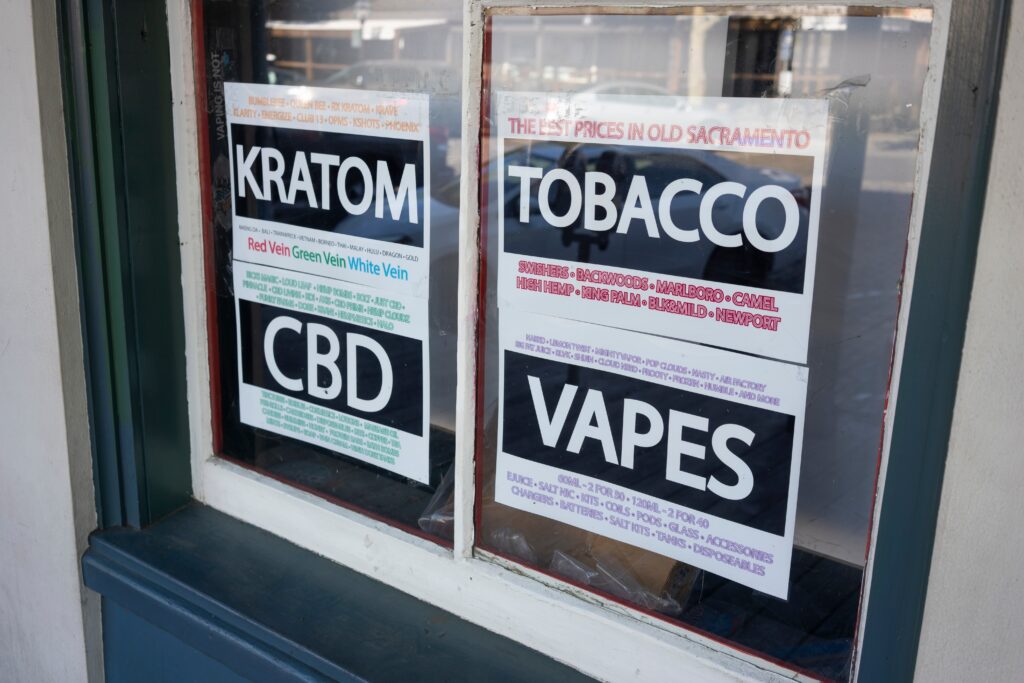 A store window with advertising signs of kratom, tobacoo, CBD, vapes and 7-OH kratom products.