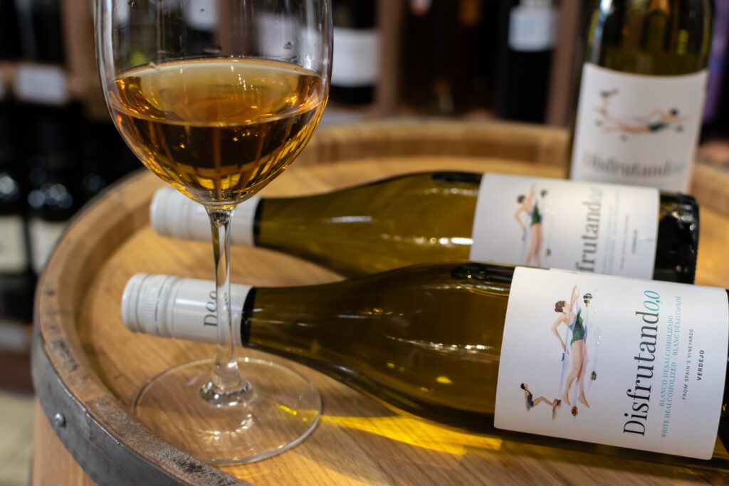Two bottles and a glass of white non alcoholic wine on top of a wine barrel.