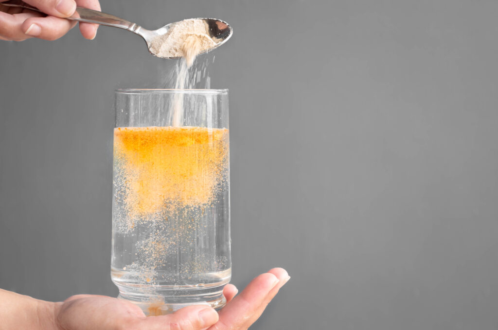 A person holding a glass of water pouring some sort of yellow powder to make a detox drink for a drug test.