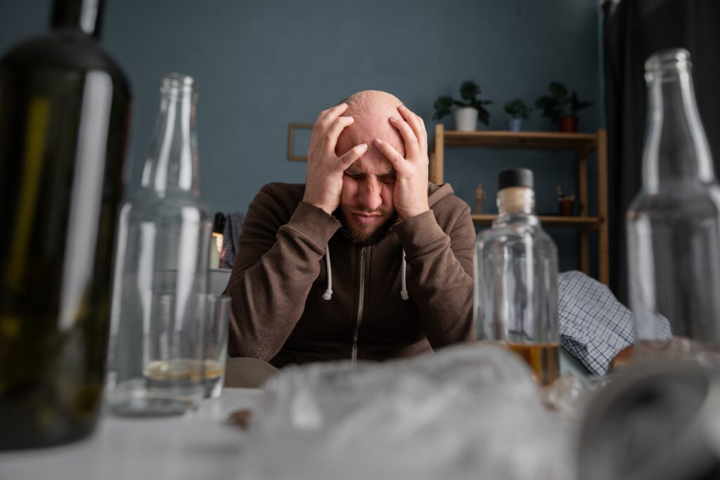 A frustrated alcoholic man surrounded by empty alcohol bottles is experiencing how alcohol is messing with his hormones.