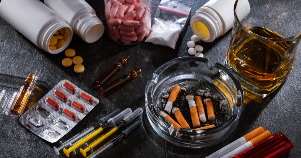 Alcohol, pills, powdered drugs and nicotine cigarettes laying on top of a table and all some of the most difficult drugs to quit.