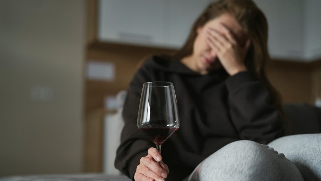A young woman holding a glass of wine is drinking alone and represents one of the subcategories of types of alcoholics.