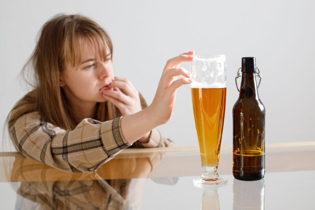 A young women with alcohol cravings torn between her sobriety and drinking a beer that has been poured out in front of her.