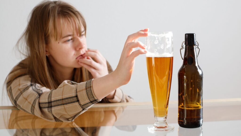 A young women with alcohol cravings torn between her sobriety and drinking a beer that has been poured out in front of her.