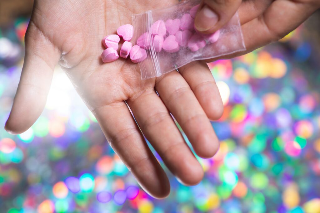 A person pouring pink heart shaped molly pills onto their hand and wondering is molly legal in California.