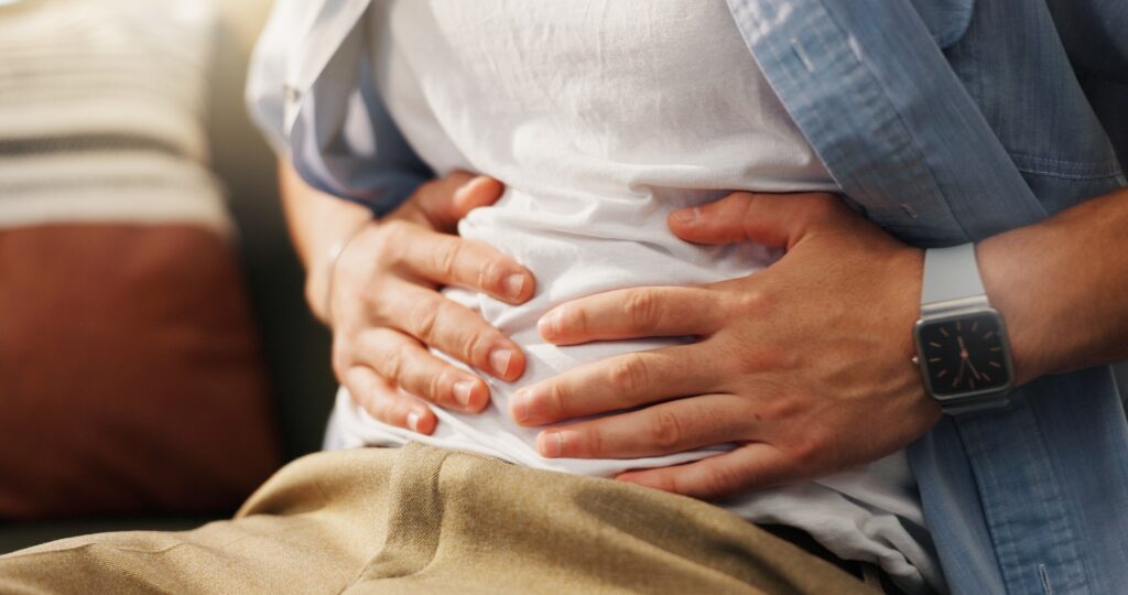 A man holding his stomach after drinking and wondering how long for alcohol bloat to go away.