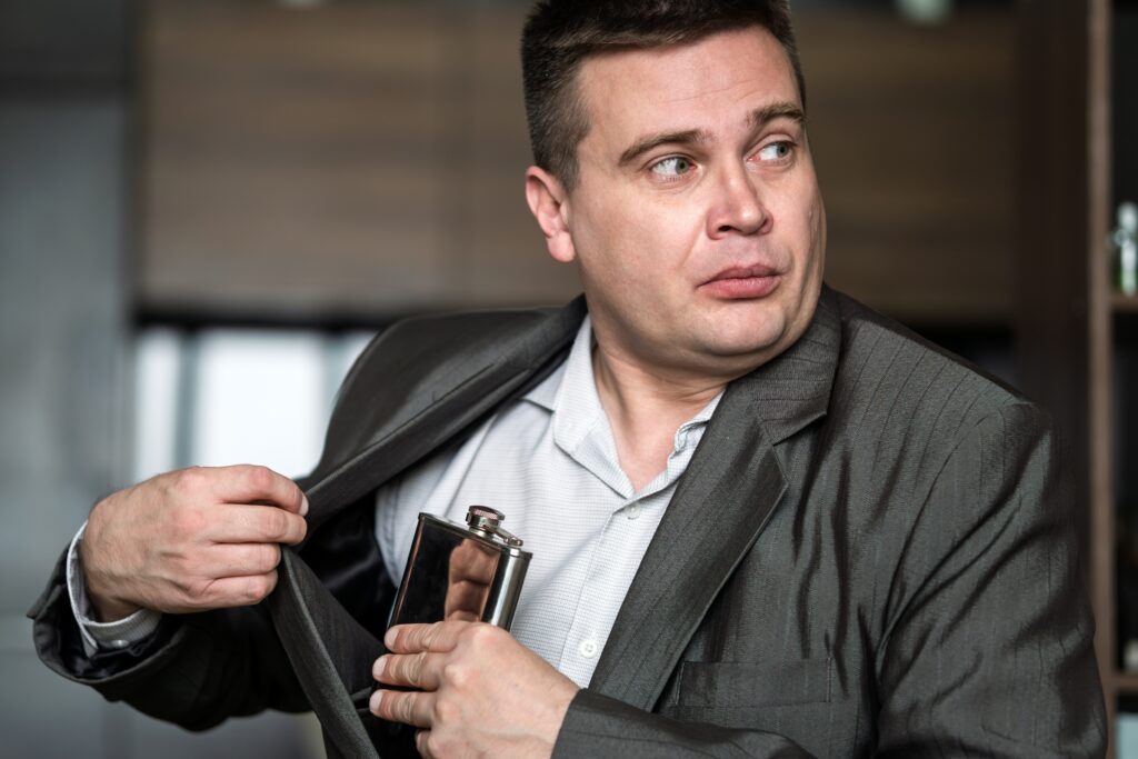 A man who is a closet alcoholic hiding a flask in his suit jacket pocket.