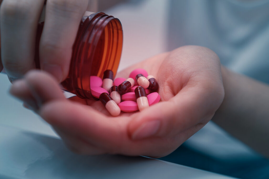 A person pouring out various pink pills and tablets into their hand representing the different between Klonopin and Xanax.
