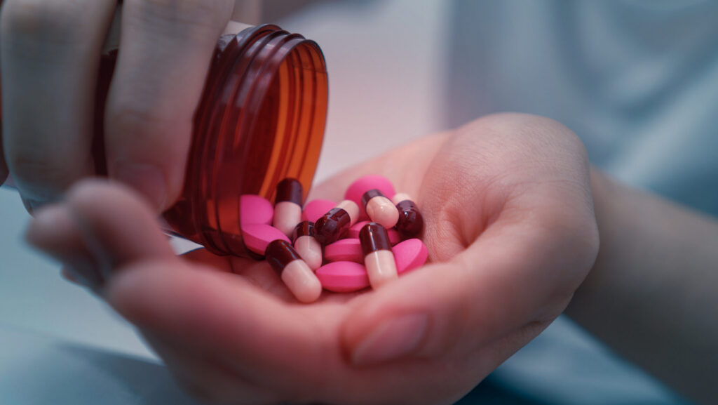 A person pouring out various pink pills and tablets into their hand representing the different between Klonopin and Xanax.