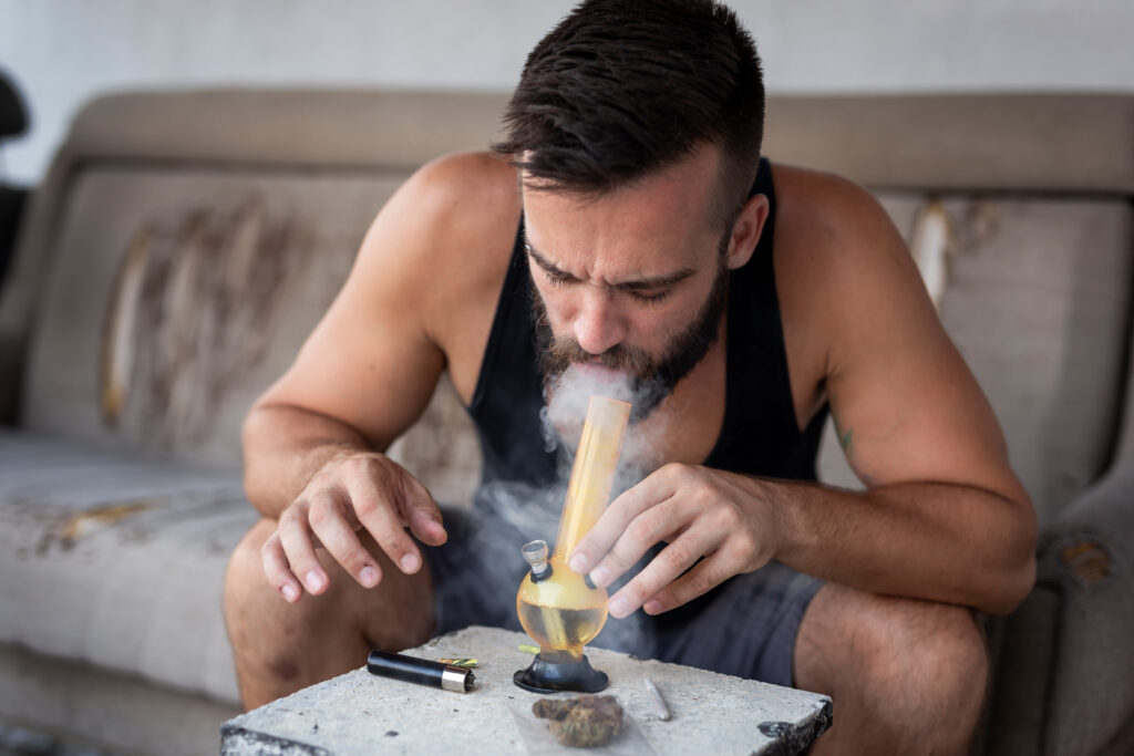 A young man smoking a pot bong also wondering what are the symptoms of greening out.