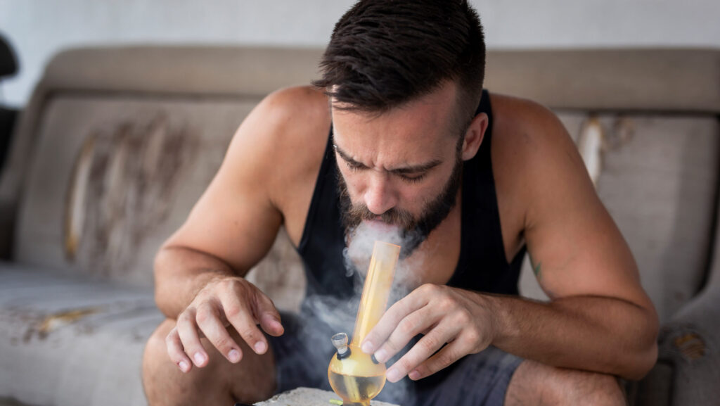 A young man smoking a pot bong also wondering what are the symptoms of greening out.