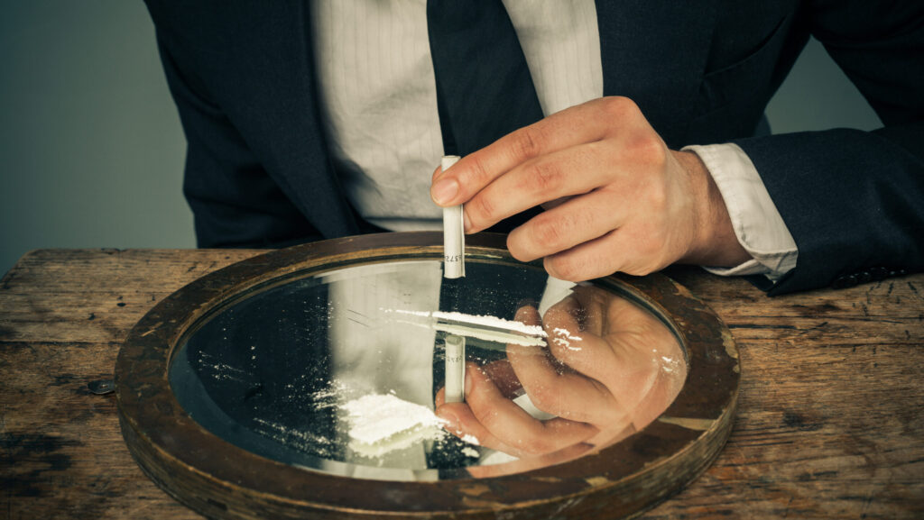 A man about to inhale a line of cocaine, but is weary because he is unsure if cocaine can make you poop.