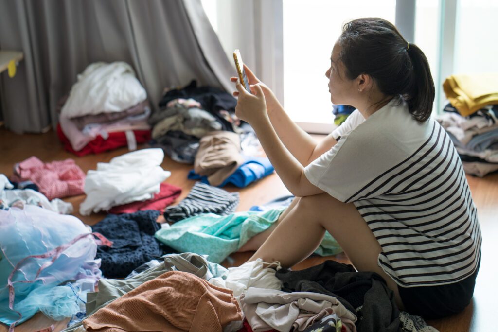 Young woman with substance addiction sitting on the floor surrounded by clothes deciding what to pack for rehab.