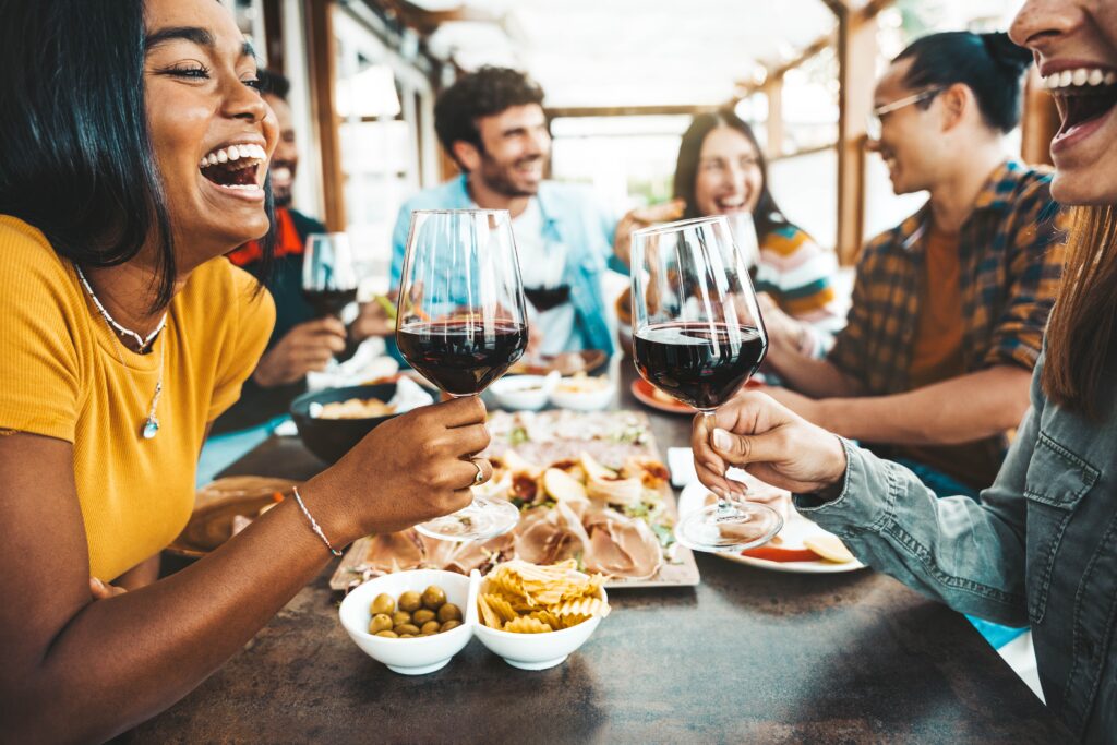 Two women and their group of friends enjoying a meal and drinks, wondering if eating makes you less drunk.