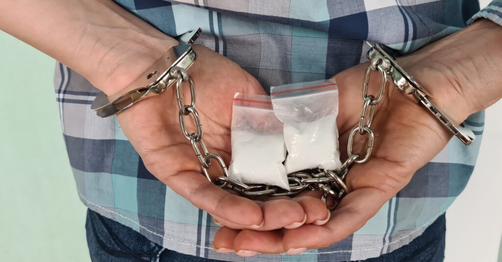A man in handcuffs holding bags of drugs represents drug treatment in prison.