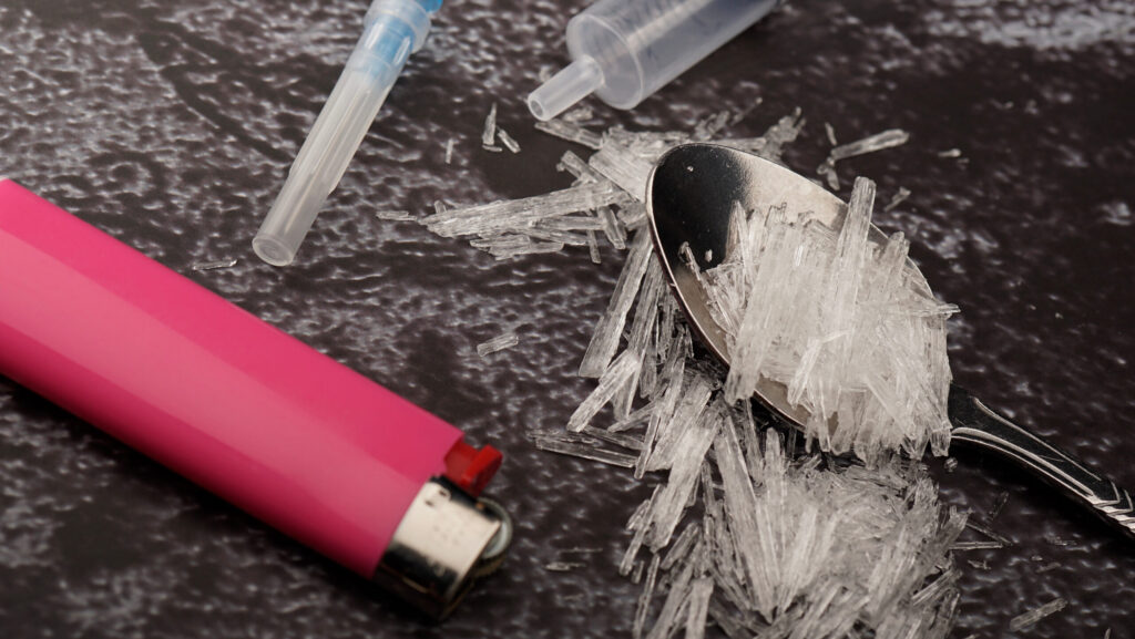 A pink lighter laying next to a spoon and shards of crystal meth.