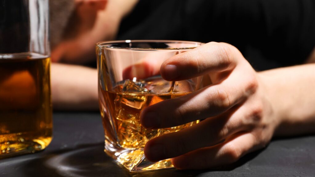 A person holding a glass of alcohol who is also struggling with alcohol neuropathy.