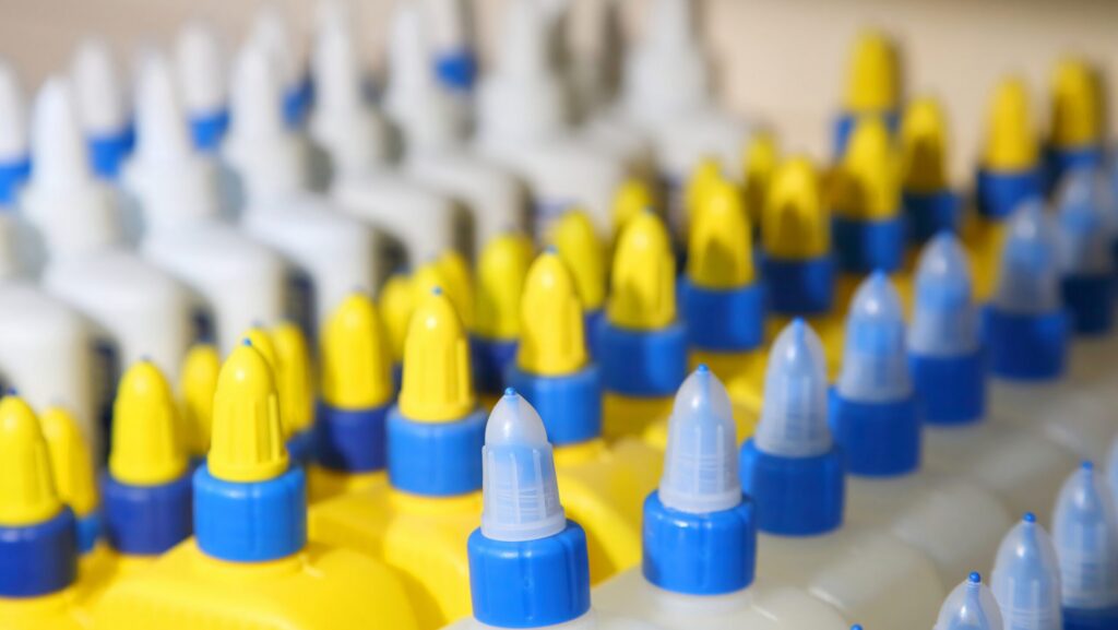 Rows of yellow, blue and white colored glue bottles lined up representing the long term effects of sniffing glue.