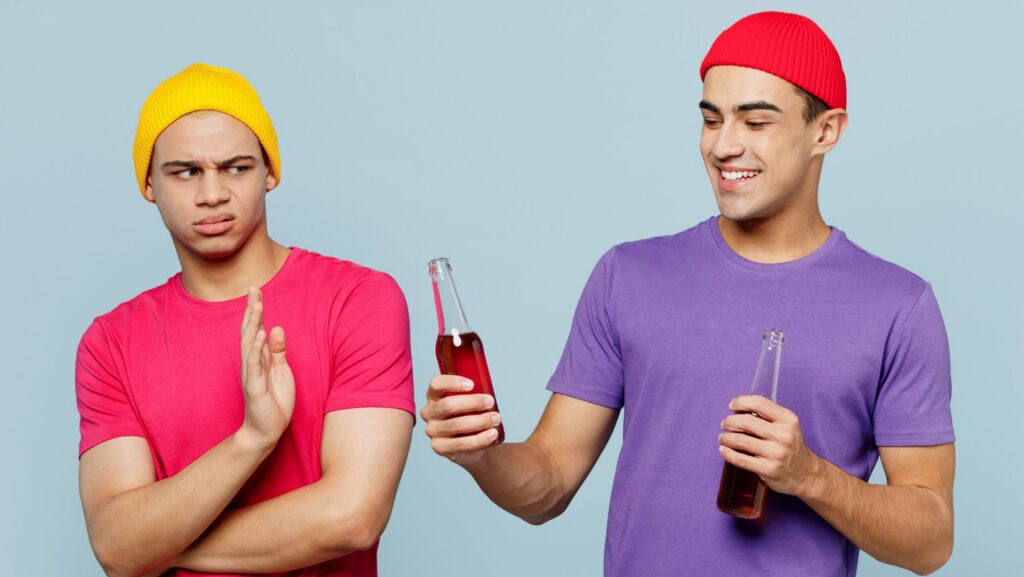 A young man rejecting alcoholic drink from his friend because he is practicing how to stay sober.