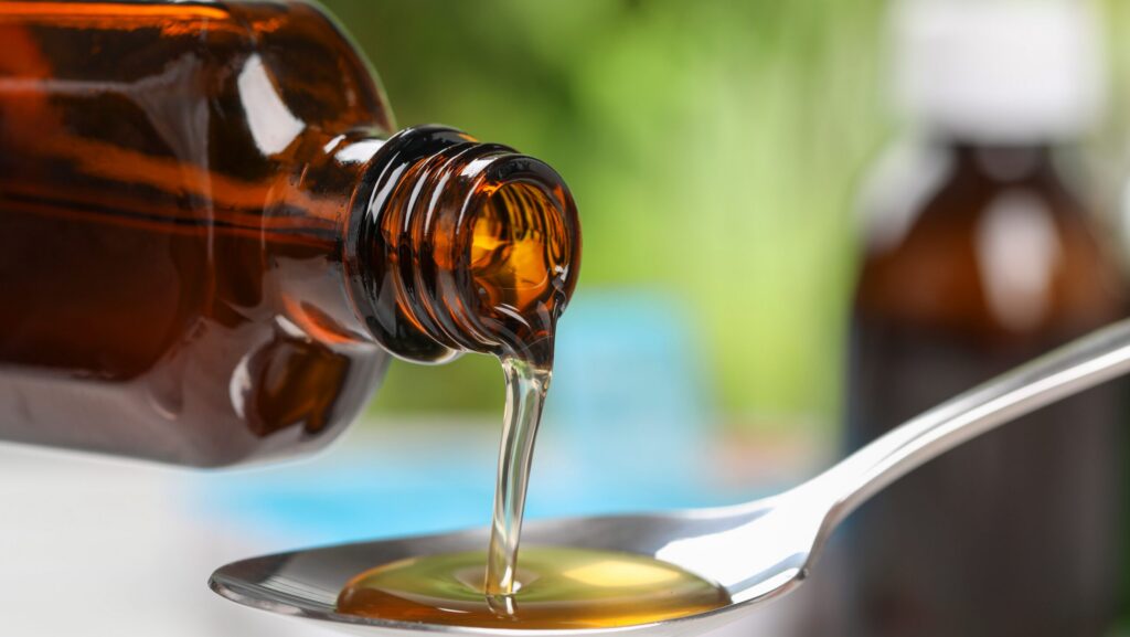 An amber jar of stilpane syrup being poured into a spoon.
