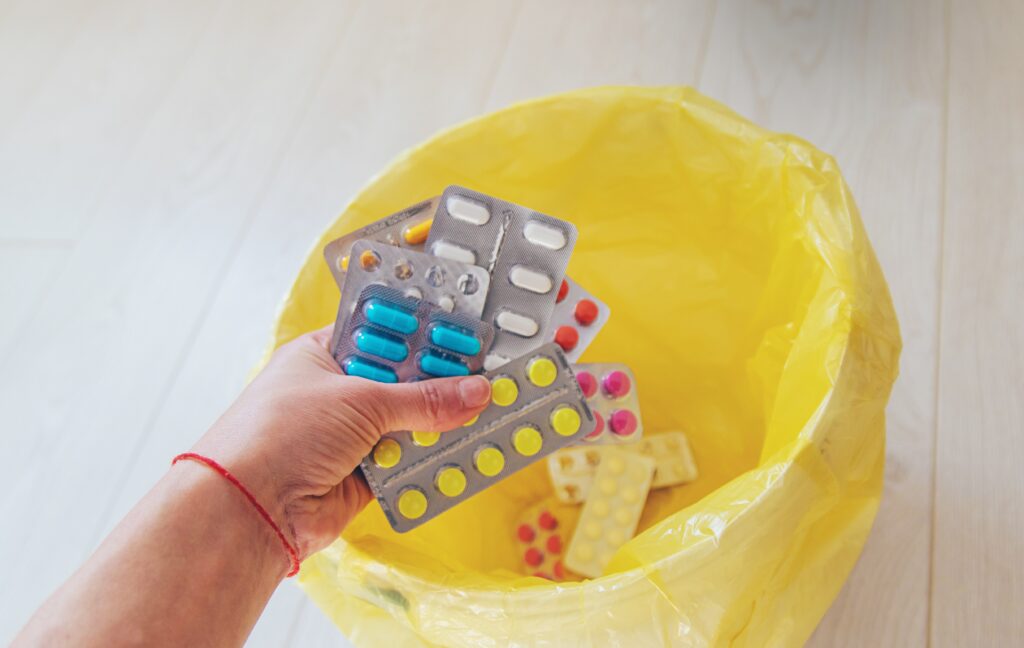 A person throwing out medications into the trash because she is wondering do drugs expire.