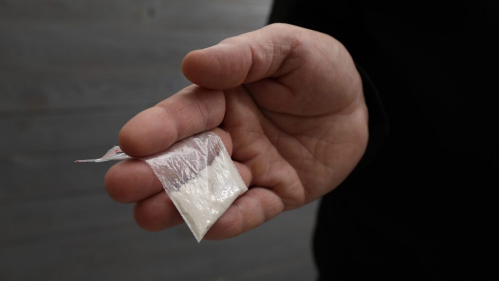 A person holding a small baggie of powdered cocaine measuring to be about na 8 ball of coke.