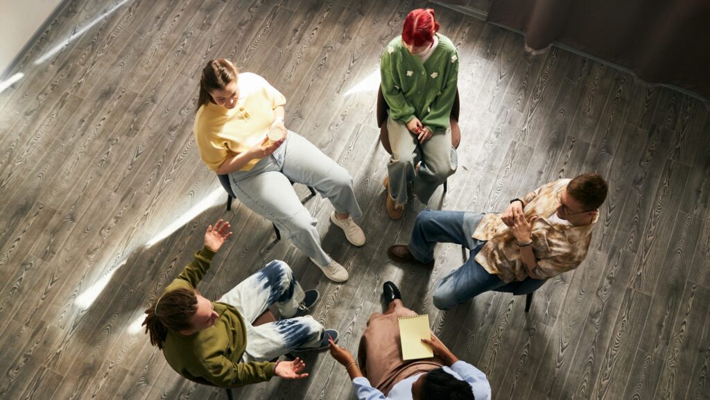 A group of young people sitting in a circle in group therapy for drug addiction.