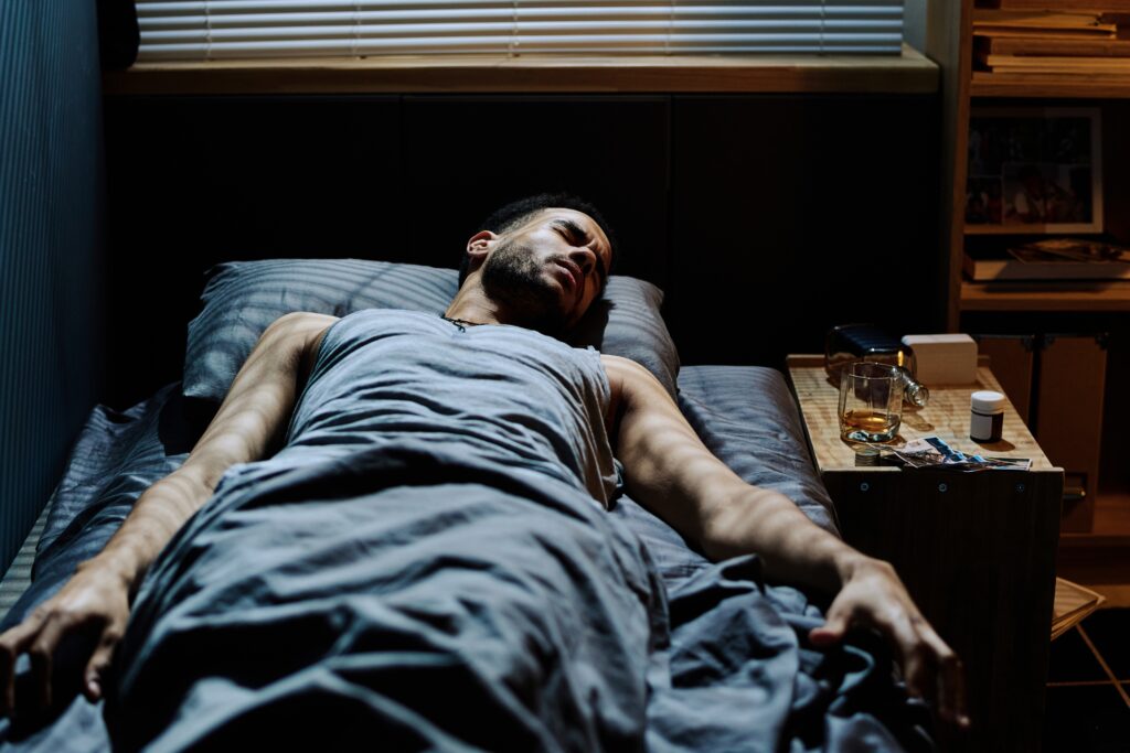 A young man in bed experiencing disturbed sleep and nightmares due to alcohol use.