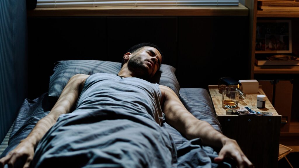 A young man in bed experiencing disturbed sleep and nightmares due to alcohol use.