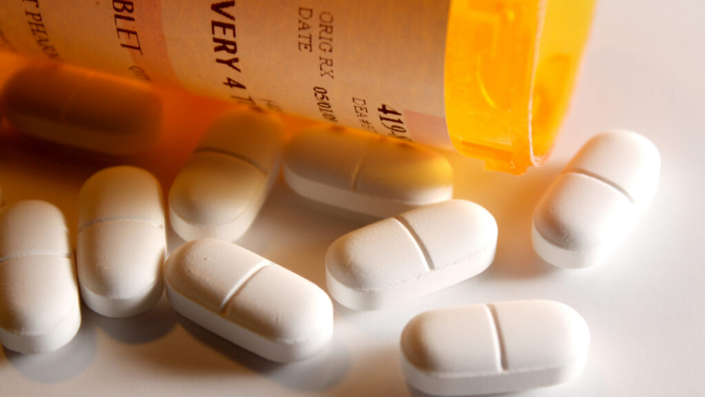 A prescription pharmacy bottle with white Percocet pills spilled out on a table.