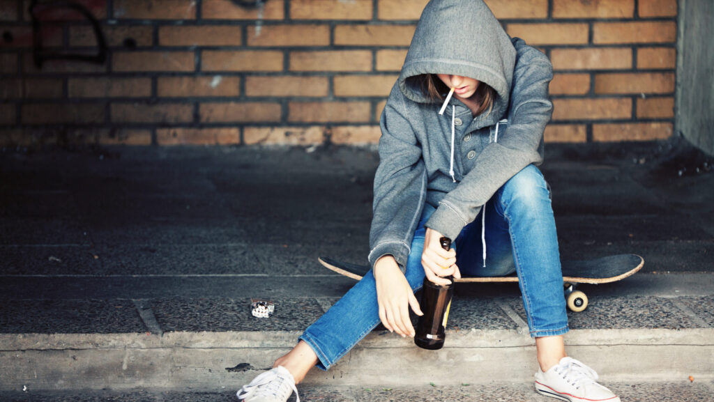 A teen girl with a cigarette in her mouth holding a bottle of alcohol represents the use of gateway drugs.