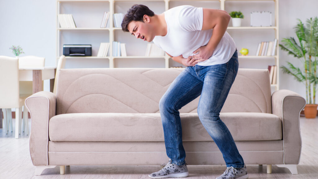 A man bent over holding his stomach because he is experiencing alcohol effects on the pancreas.
