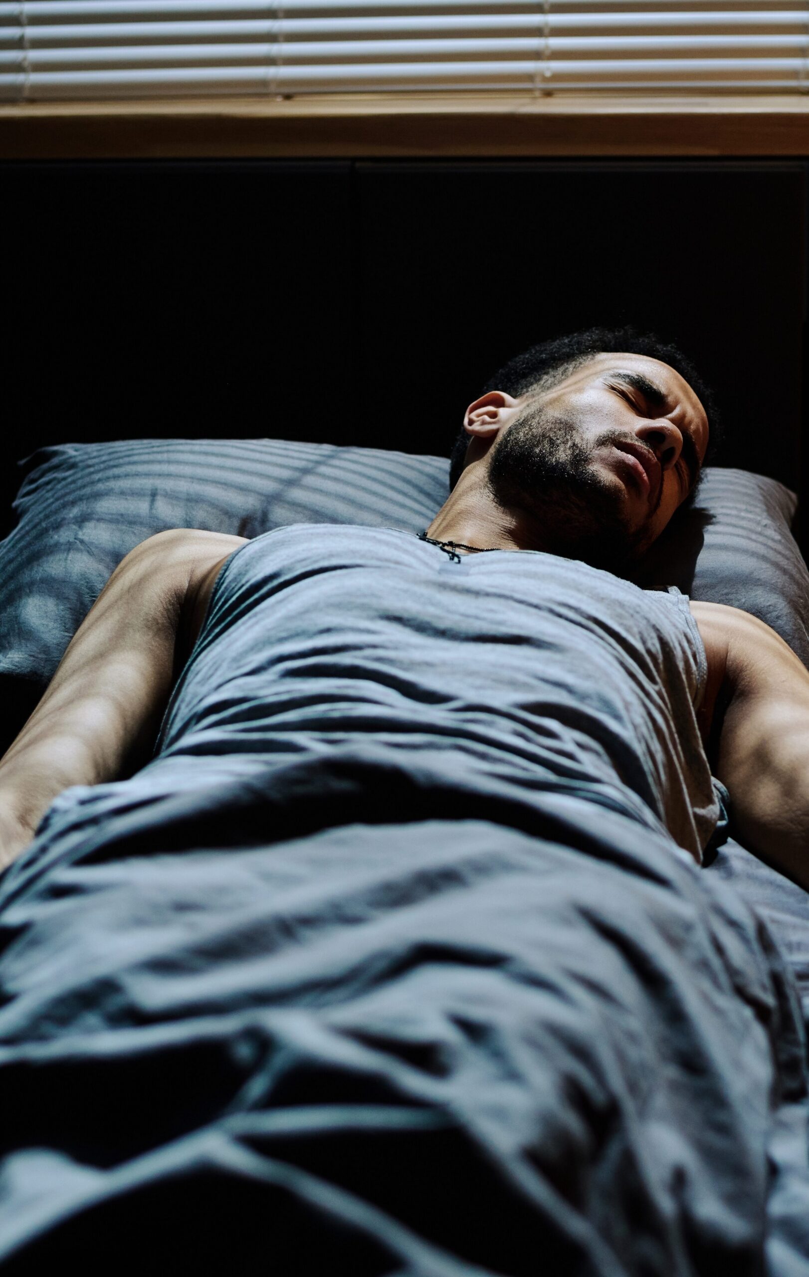A young man in bed experiencing disturbed sleep and nightmares due to alcohol use.