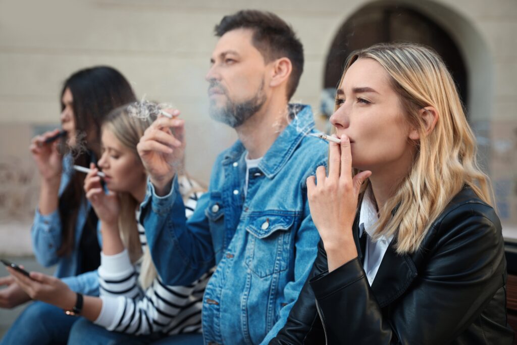 A group of people smoking cigarettes and vapes on their break at work may be experiencing nicotine addiction symptoms that caused them to relapse in their tobacco use.