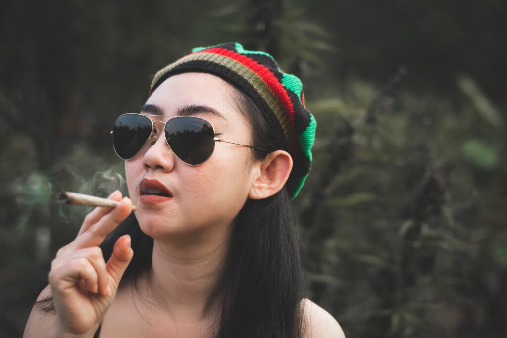 A young woman smoking a marijuana joint covering her eyes because she doesn't know how long does red eyes last from weed.
