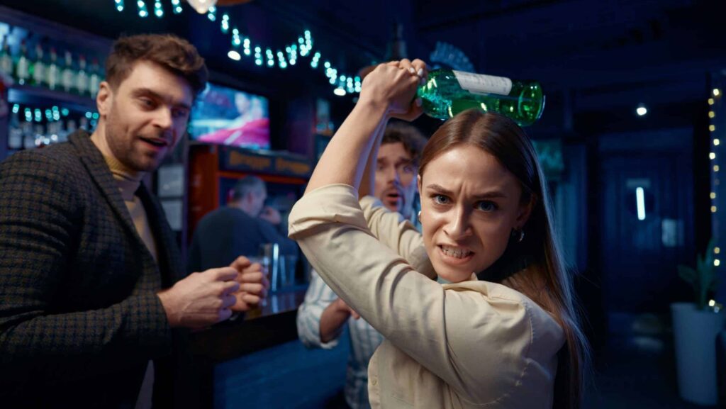 A woman who becomes angry drunk when consuming alcohol holds a bottle about to strike someone.